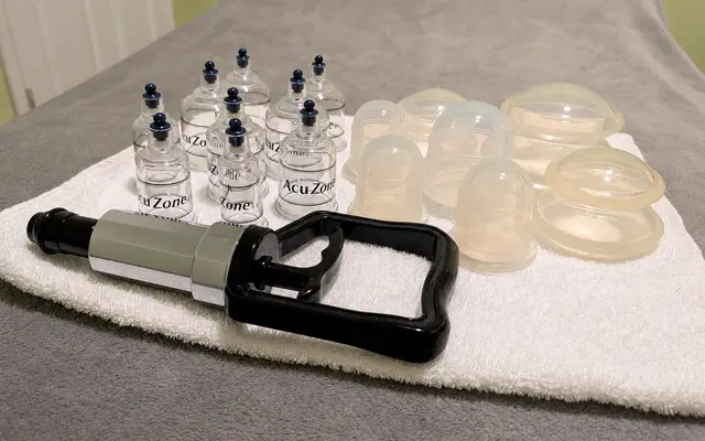 Cupping therapy cups and a handheld suction pump arranged on a massage table.